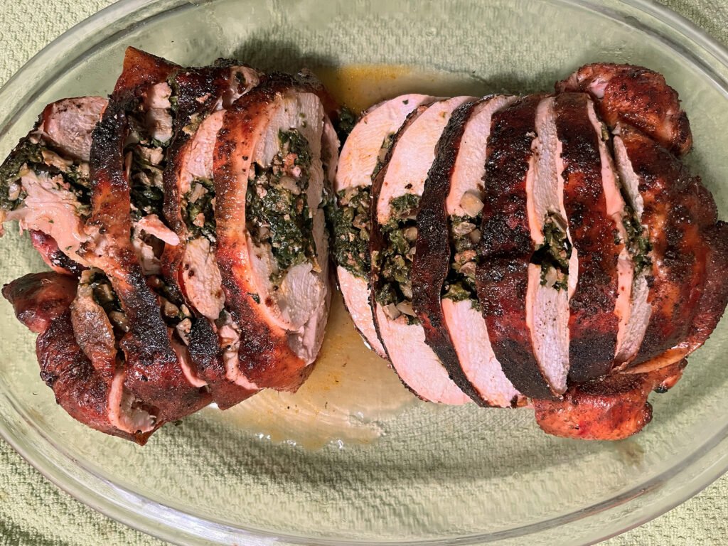 Sliced stuffed whole chicken with a browned, charred crust rests on a glass platter, showing a juicy pink interior and a hearty, inviting meal.