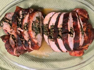 Sliced stuffed whole chicken with a browned, charred crust rests on a glass platter, showing a juicy pink interior and a hearty, inviting meal.