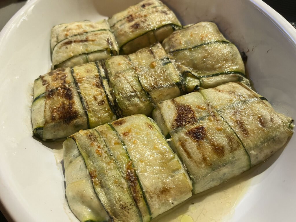 Seven zucchini-wrapped parcels with golden-brown grill marks in a white serving platter.
